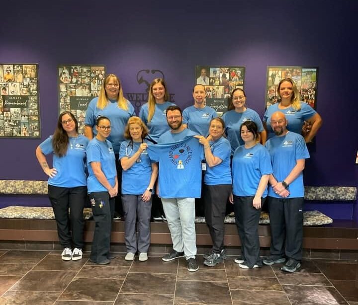 Bartels Busack Pet Hospital team members in matching blue shirts posing together in front of a purple wall of pet photos
