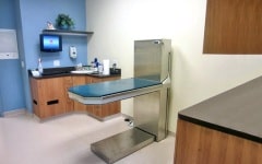 Exam room with a stainless steel lift table, counter and wall-mounted monitor