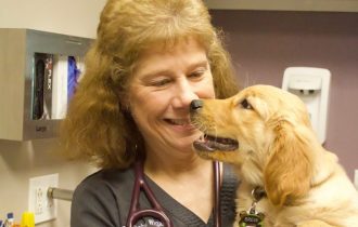 Dr. Debra Wigal smiles as a golden retriever puppy leans in close in an exam room